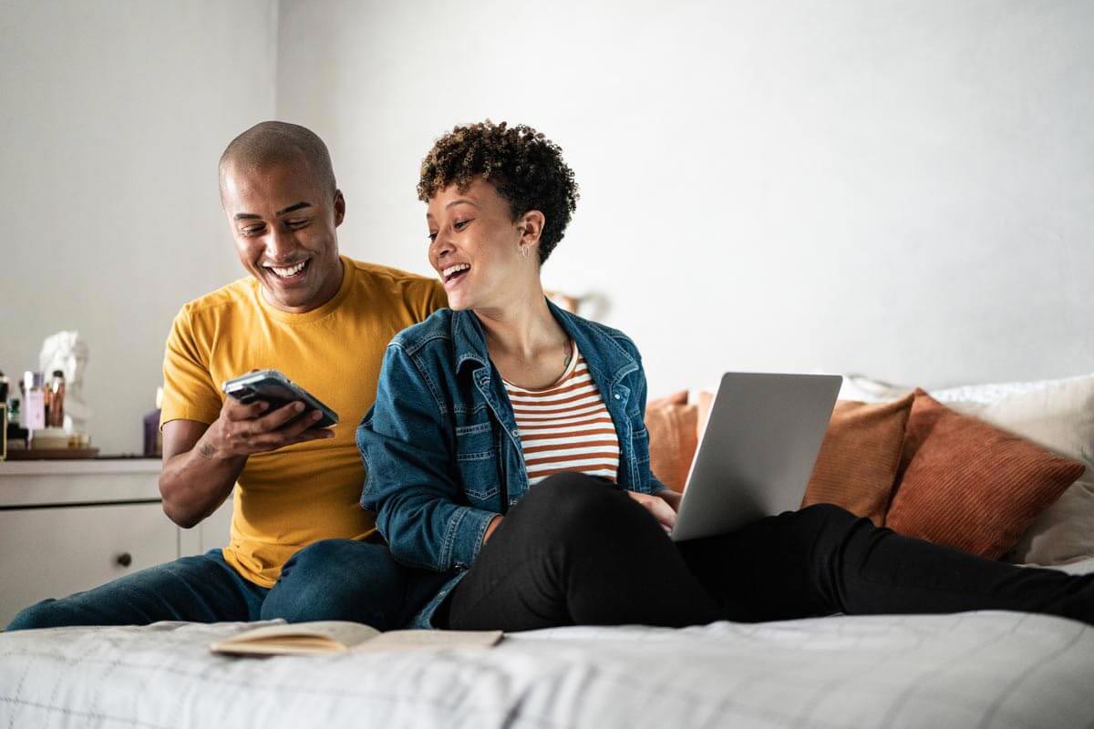 man and woman laying on bed and smiling while looking at phone together